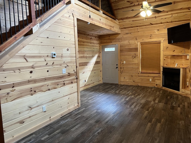 unfurnished living room featuring ceiling fan, a towering ceiling, dark wood-type flooring, and wooden walls