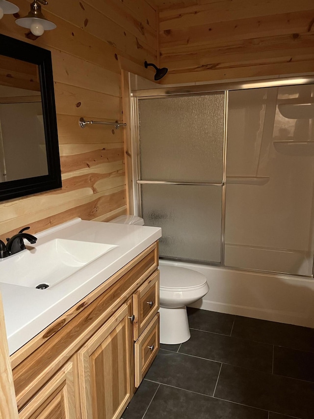 full bathroom with combined bath / shower with glass door, tile patterned floors, vanity, toilet, and wood walls