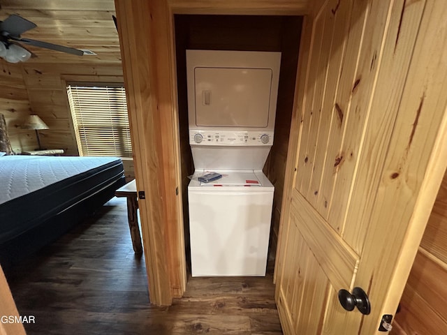 clothes washing area with ceiling fan, wood walls, dark hardwood / wood-style flooring, and stacked washer / dryer