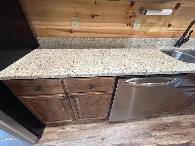 interior details featuring light stone counters, dishwasher, dark brown cabinets, and sink