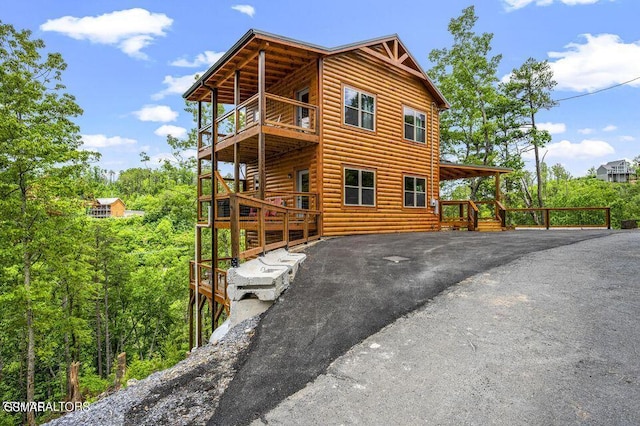 view of side of home featuring driveway, log veneer siding, and a balcony