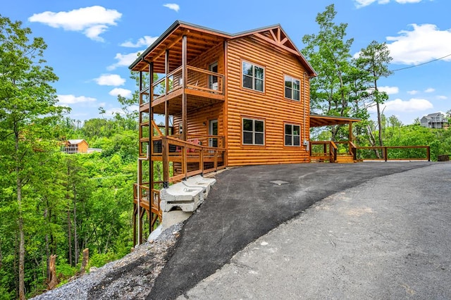 view of home's exterior with a balcony, driveway, and log veneer siding