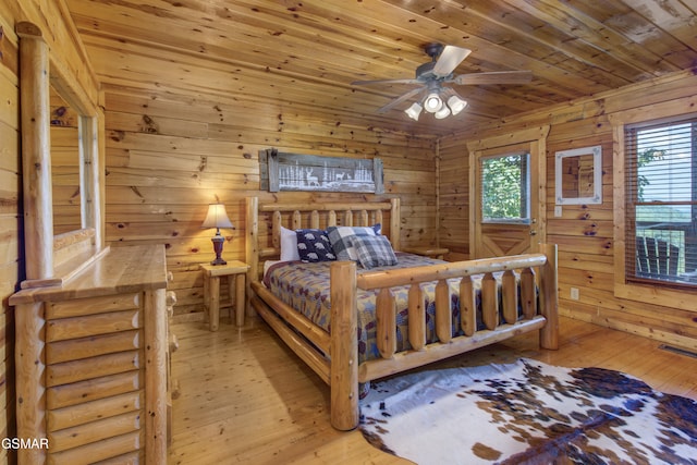 bedroom with wooden walls, multiple windows, wooden ceiling, and light wood-type flooring