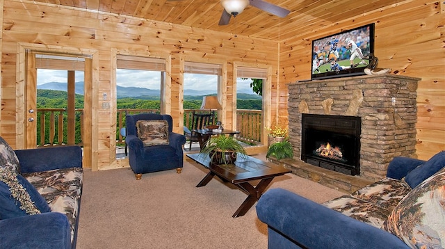 carpeted living room with a stone fireplace, wooden walls, ceiling fan, and wood ceiling