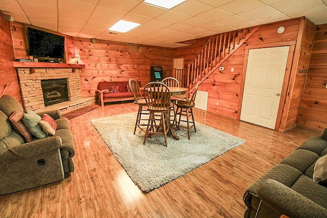 dining area featuring hardwood / wood-style floors, wood walls, and a stone fireplace