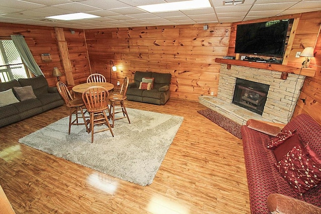 living room with a paneled ceiling, hardwood / wood-style flooring, and a stone fireplace