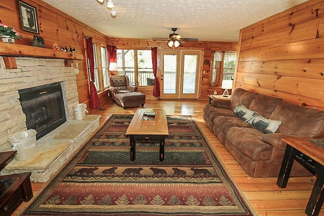 living room featuring a fireplace, wood-type flooring, a textured ceiling, and wooden walls