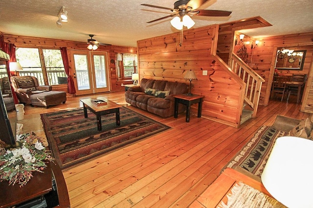 living room with ceiling fan, wooden walls, a textured ceiling, and hardwood / wood-style flooring