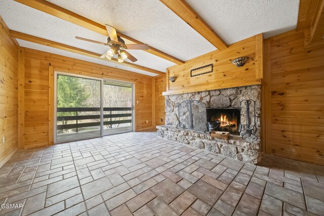 260 Roaring Fork Rd Unit 217, Gatlinburg, TN 37738 - unfurnished living room featuring a textured ceiling, ceiling fan, a stone fireplace, wooden walls, and beam ceiling