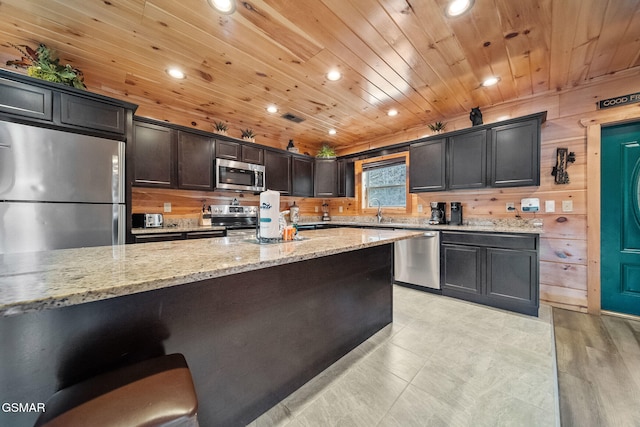 kitchen with wood walls, wooden ceiling, sink, light stone countertops, and stainless steel appliances