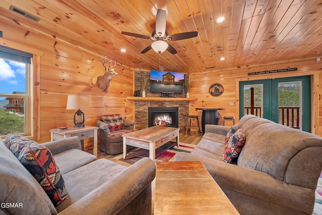 living room featuring french doors, a stone fireplace, hardwood / wood-style flooring, ceiling fan, and wood ceiling