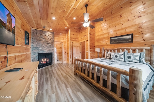 bedroom featuring wood walls, wooden ceiling, ceiling fan, a fireplace, and wood-type flooring