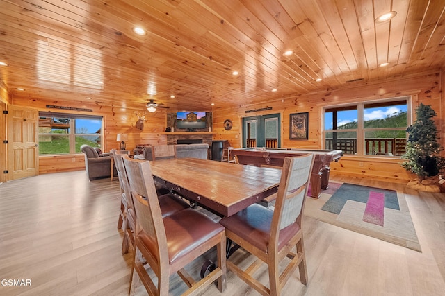 dining space with a stone fireplace, wood walls, ceiling fan, and a healthy amount of sunlight