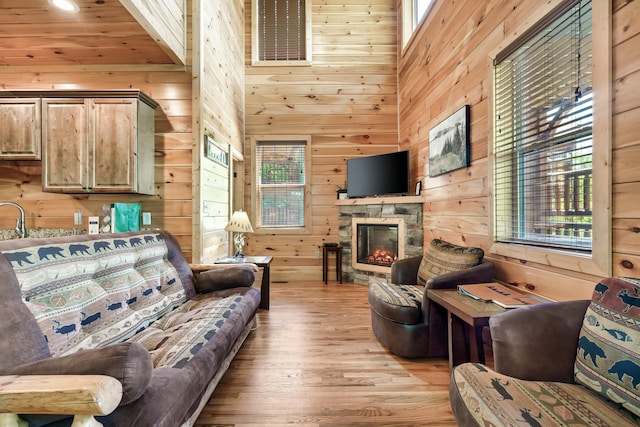 living room featuring a high ceiling, light wood-type flooring, a stone fireplace, and wood walls