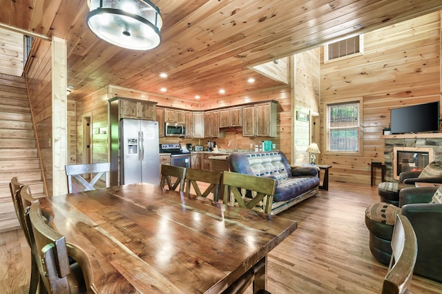 dining room with a fireplace, light hardwood / wood-style floors, wooden ceiling, and wood walls