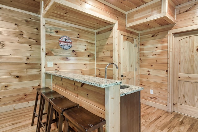 bar featuring light stone countertops, light wood-type flooring, wooden walls, and sink