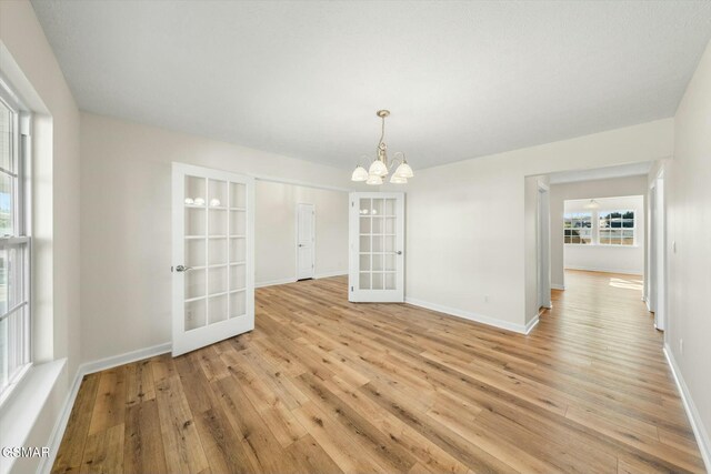 unfurnished dining area with a chandelier, light wood-type flooring, and french doors