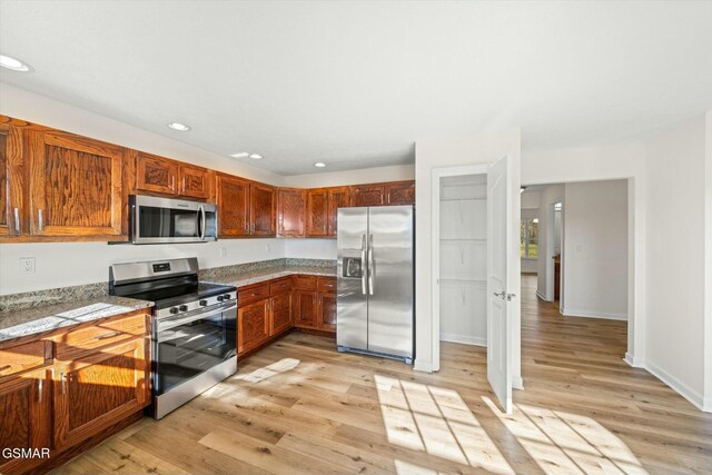 kitchen featuring appliances with stainless steel finishes, light hardwood / wood-style floors, and light stone counters