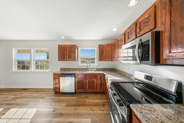 kitchen featuring sink, light wood-type flooring, a textured ceiling, appliances with stainless steel finishes, and light stone counters