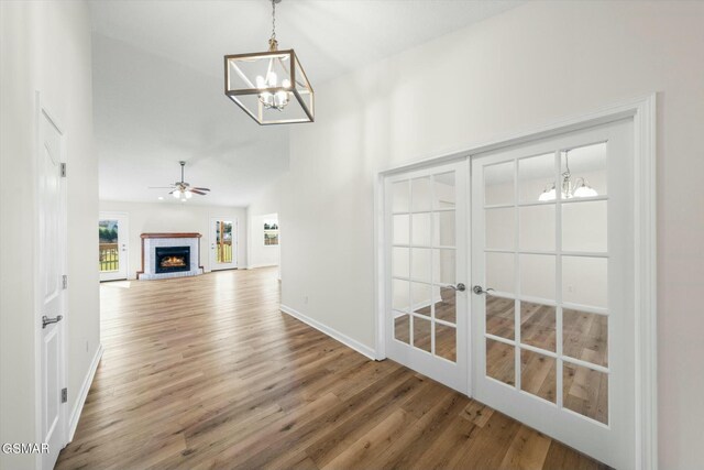 unfurnished living room featuring french doors, a brick fireplace, ceiling fan with notable chandelier, vaulted ceiling, and hardwood / wood-style flooring