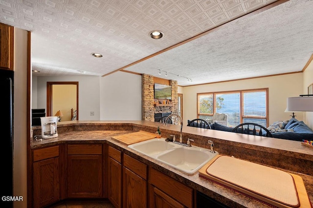 kitchen featuring track lighting, ornamental molding, a textured ceiling, sink, and a fireplace