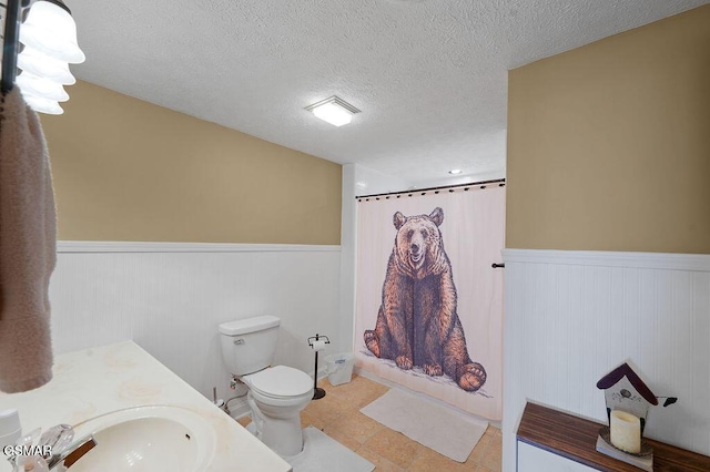 full bathroom featuring tile patterned floors, a textured ceiling, toilet, shower / bath combo with shower curtain, and vanity