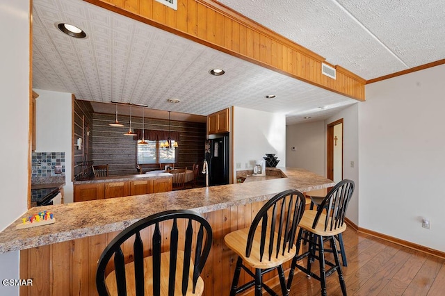 kitchen featuring hardwood / wood-style floors, backsplash, black refrigerator, a textured ceiling, and kitchen peninsula