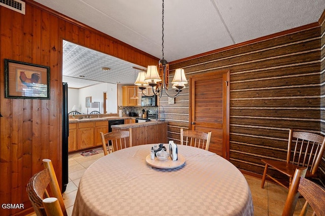 dining room with sink, wooden walls, light tile patterned floors, ornamental molding, and a notable chandelier