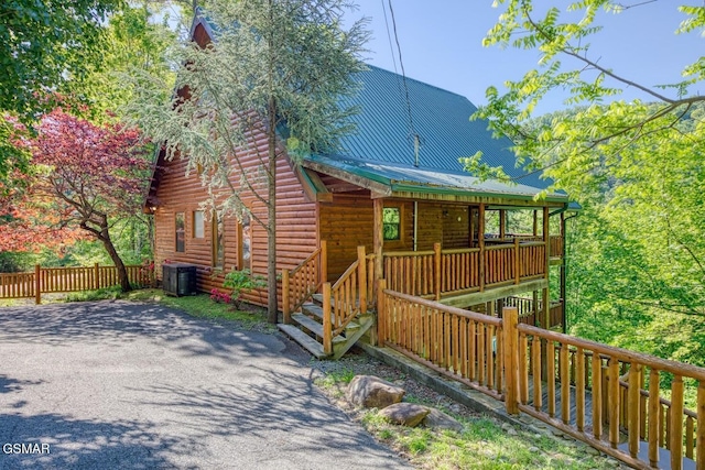 view of front of property featuring central AC unit, faux log siding, a porch, metal roof, and fence