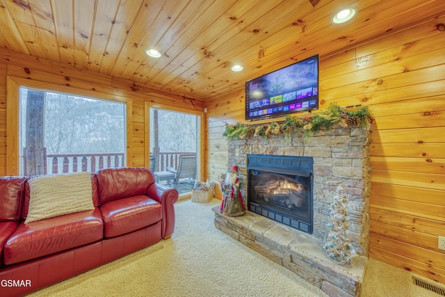 carpeted living room featuring a wealth of natural light, wood walls, and a stone fireplace