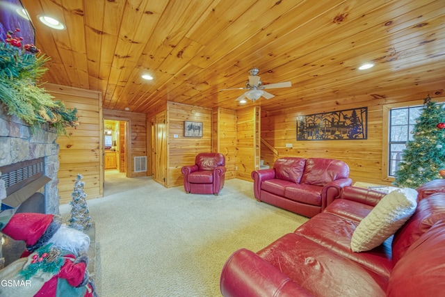 living room featuring carpet, a stone fireplace, wooden walls, ceiling fan, and wooden ceiling