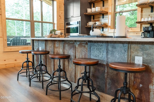 bar with a healthy amount of sunlight, light hardwood / wood-style flooring, oven, and wooden walls