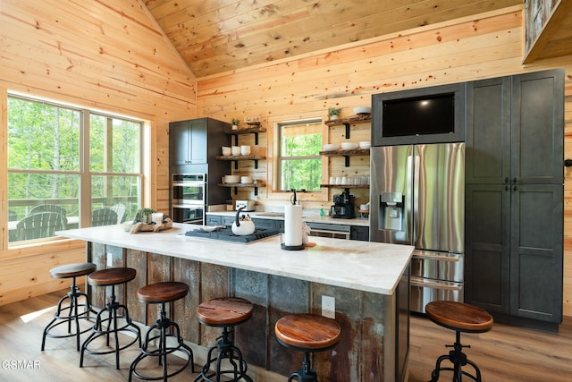 kitchen featuring stainless steel appliances, light stone counters, wood walls, a kitchen island, and light wood-type flooring