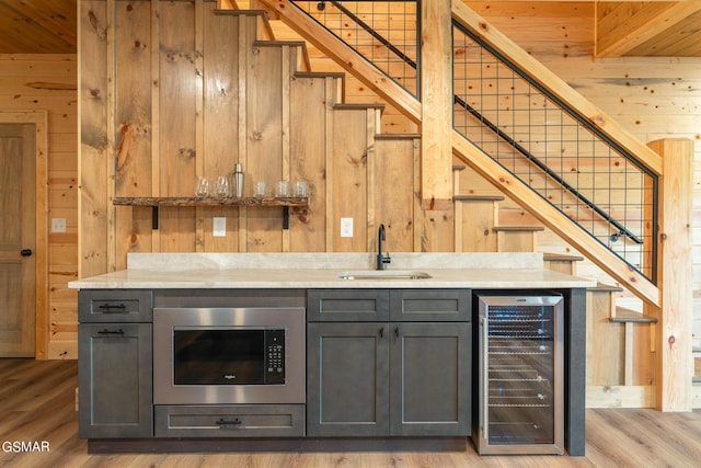 bar with gray cabinetry, wooden walls, sink, and beverage cooler