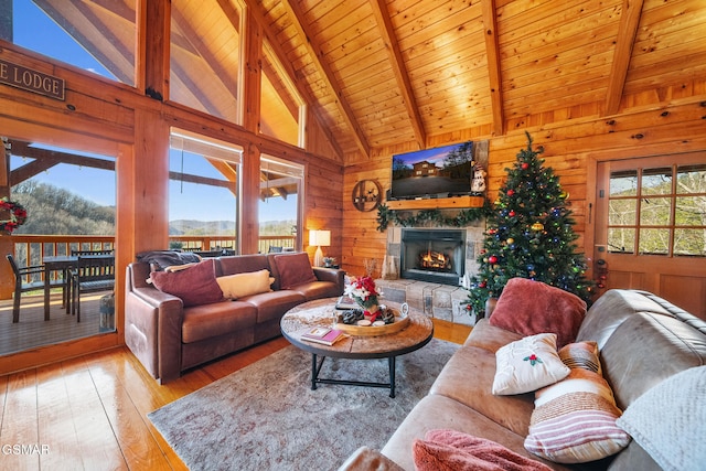 living room featuring beam ceiling, a stone fireplace, wooden ceiling, and wooden walls