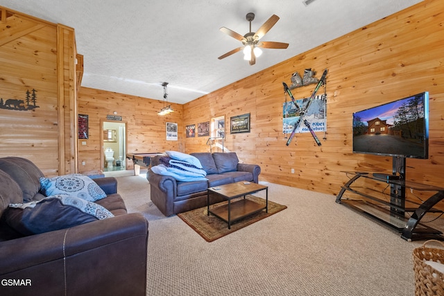 carpeted living room featuring ceiling fan, wooden walls, and a textured ceiling