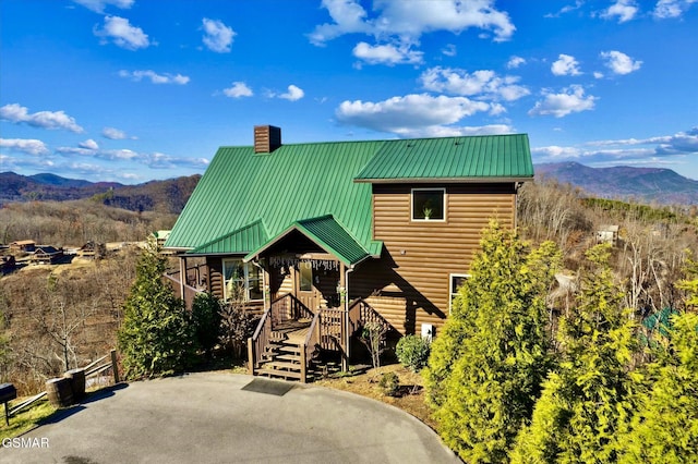 view of front facade featuring metal roof, a chimney, a mountain view, and faux log siding