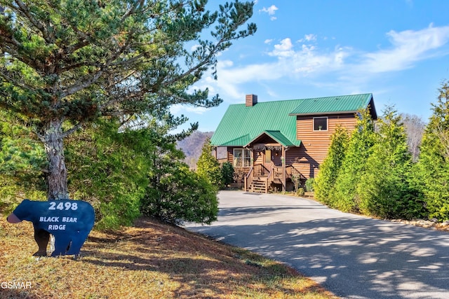 view of front of property with driveway, a chimney, metal roof, and log veneer siding