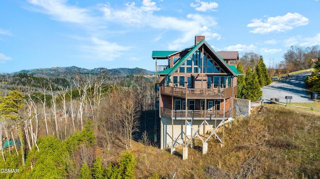 rear view of property featuring a balcony, a chimney, and metal roof