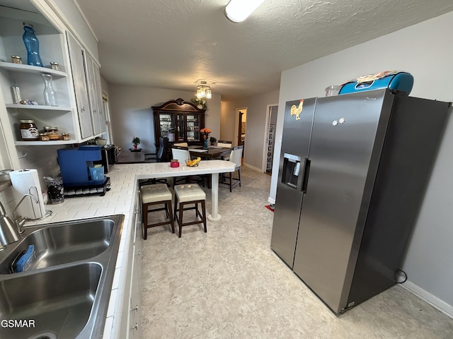 kitchen featuring stainless steel refrigerator with ice dispenser, open shelves, light countertops, a sink, and a textured ceiling