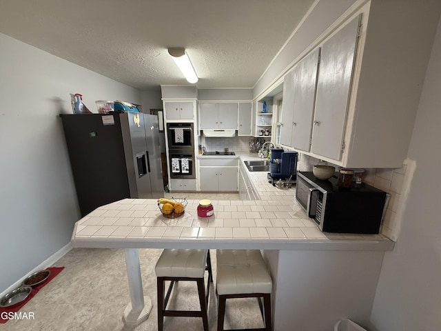 kitchen with tile countertops, tasteful backsplash, appliances with stainless steel finishes, white cabinetry, and a kitchen breakfast bar