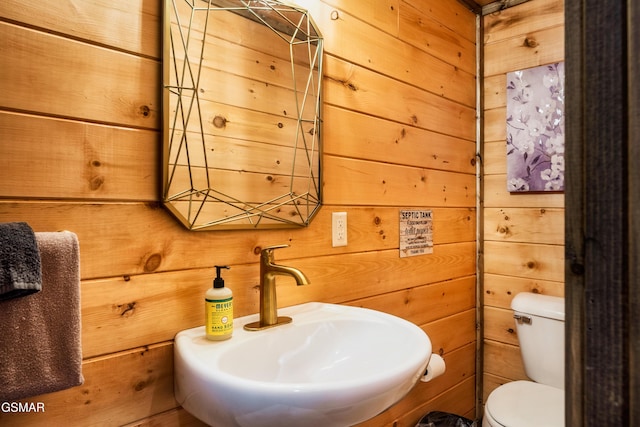 bathroom with wooden walls, sink, and toilet