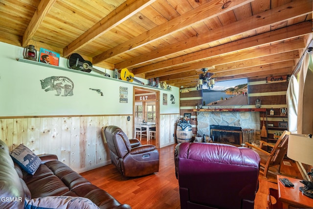 living room with wooden ceiling, a stone fireplace, beamed ceiling, and a wainscoted wall