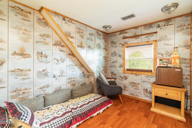 sitting room featuring visible vents, a textured ceiling, wallpapered walls, and wood finished floors