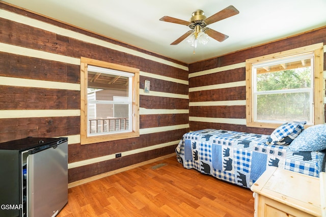 bedroom with light wood finished floors, wooden walls, and freestanding refrigerator