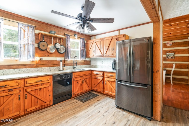 kitchen with black dishwasher, tasteful backsplash, light wood-style floors, freestanding refrigerator, and a sink
