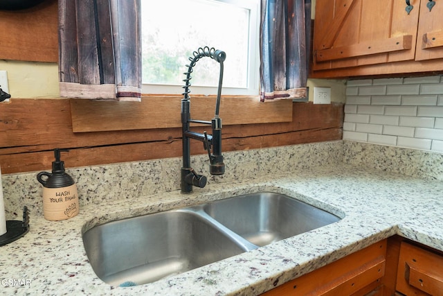 interior details with light stone countertops, backsplash, a sink, and brown cabinetry