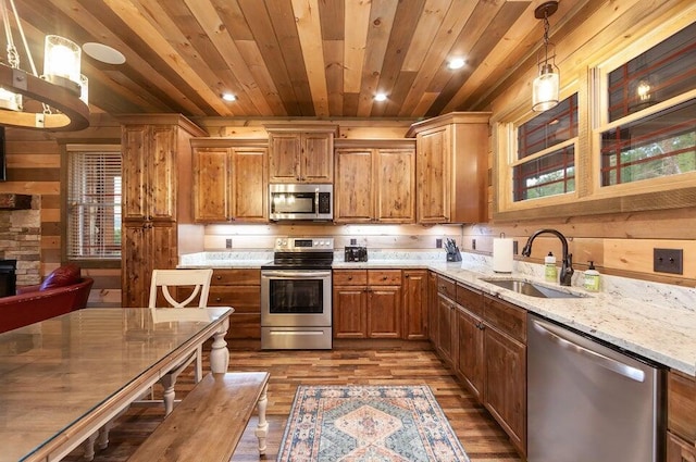 kitchen with light stone counters, stainless steel appliances, sink, pendant lighting, and dark hardwood / wood-style floors