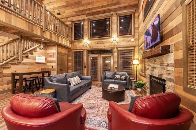 living room featuring a stone fireplace, wood walls, french doors, and a high ceiling