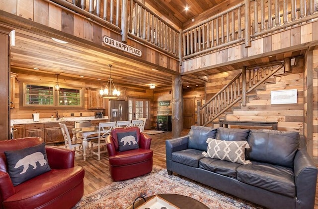 living room with a high ceiling, wood ceiling, wooden walls, an inviting chandelier, and hardwood / wood-style floors